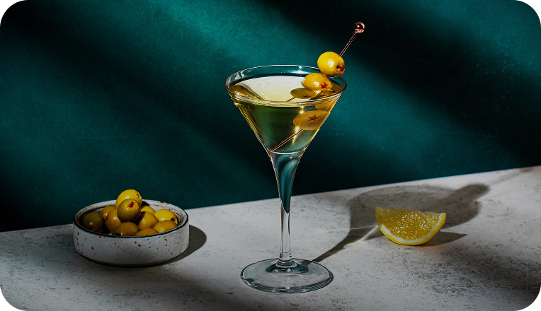Image of a cocktail, lemon wedge, and olives on a table